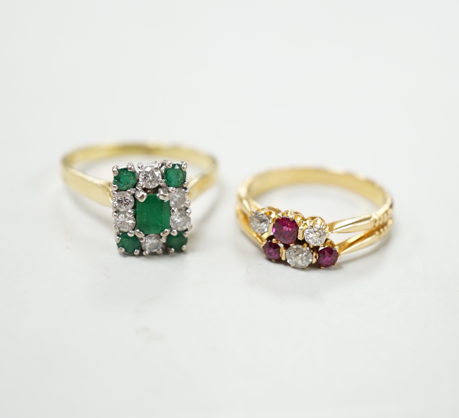 An 18ct, emerald and diamond set rectangular cluster ring, size R and an 18ct, ruby and diamond set cluster ring, size O, gross weight 8 rams.